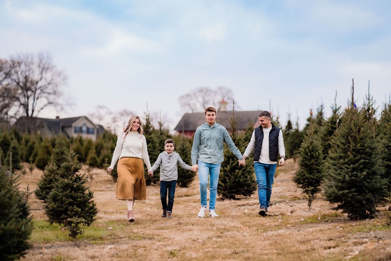 Family holding hands while running through Christmas tree farm together on sunny day.