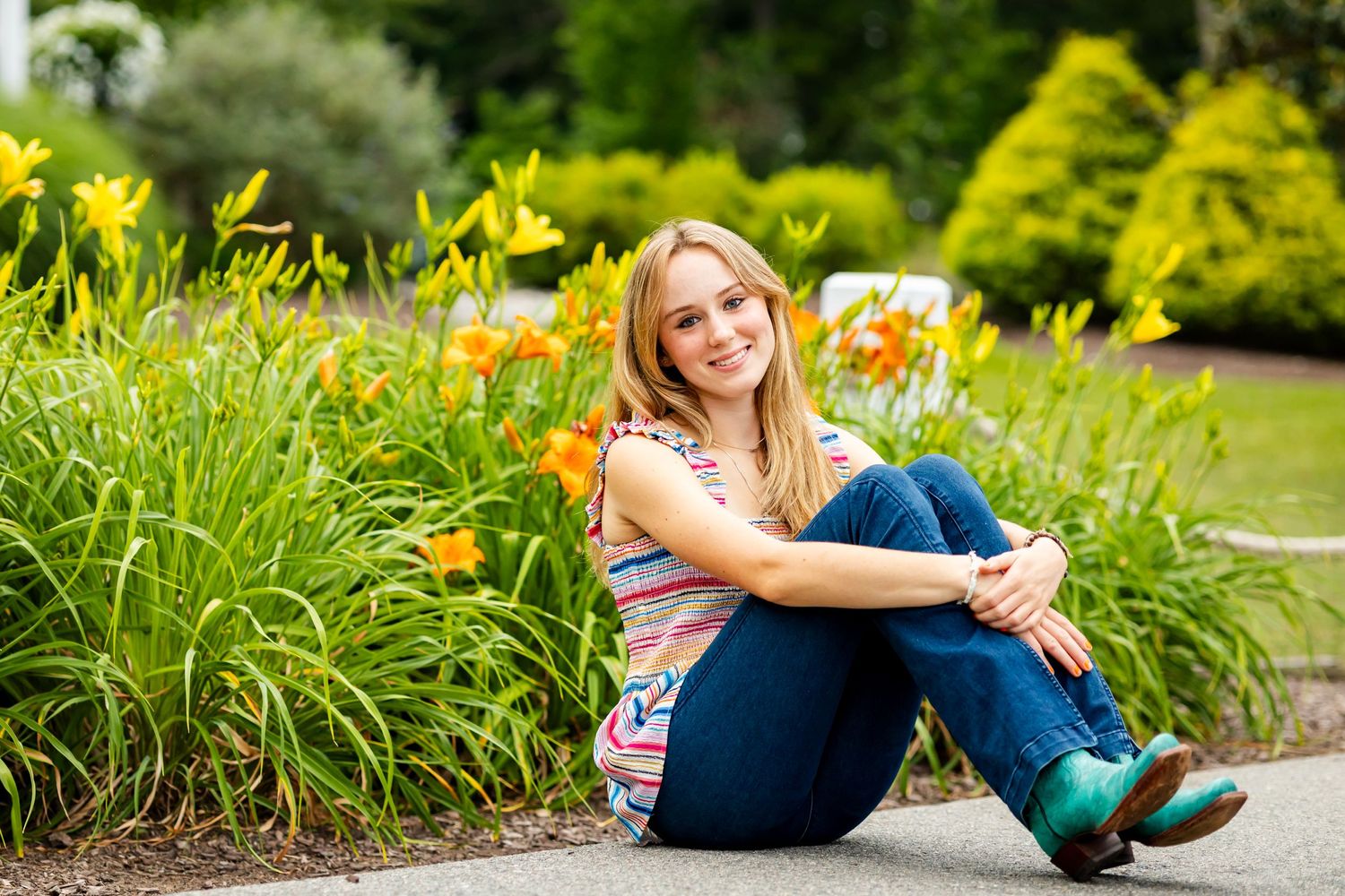 Person sitting in a garden with colorful daylilies and greenery in the background.