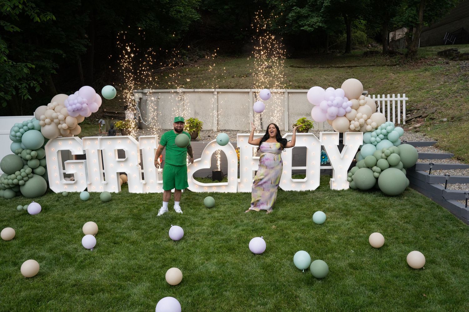 Outdoor gender reveal party setup with white letters and pastel balloon decorations.