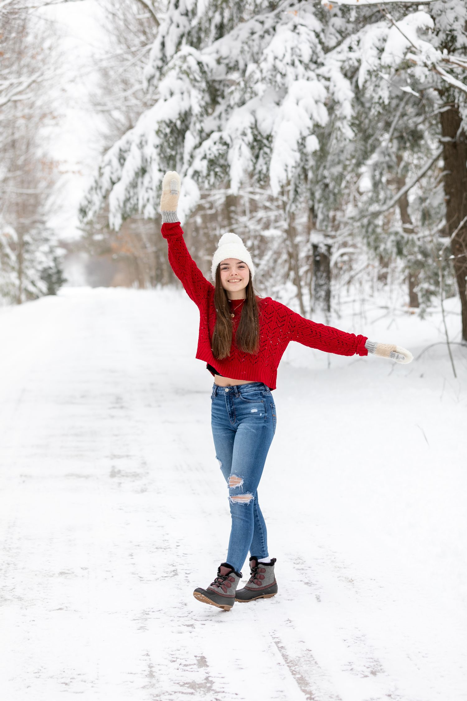 Person in bright red sweater dances playfully in snow-covered winter wonderland.