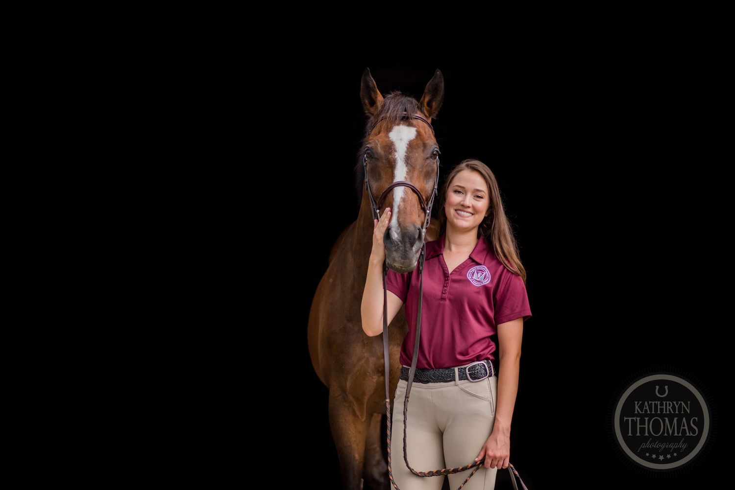 A bay horse and someone in equestrian attire pose together against black background.