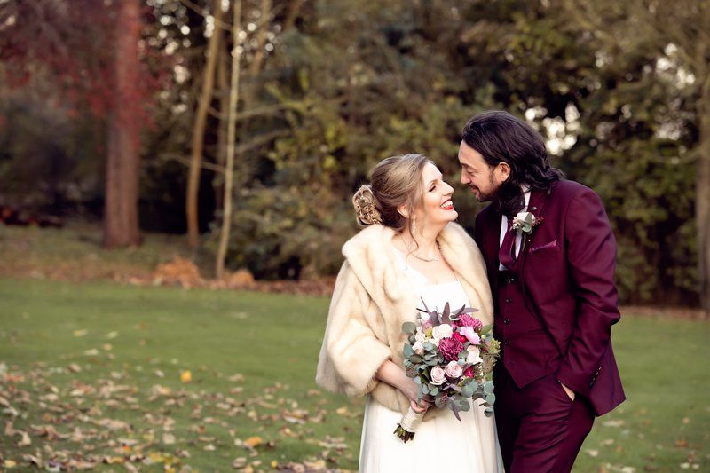 A couple shares a romantic moment in autumn garden wearing burgundy and white wedding attire.