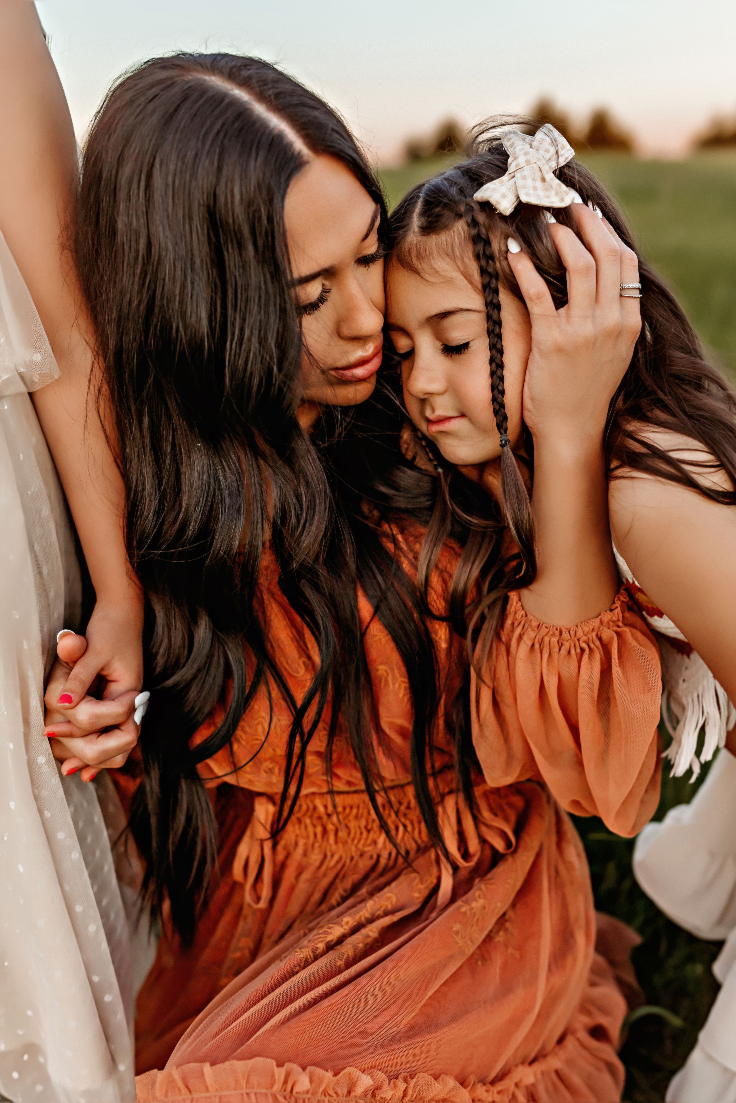 Two people in orange and white dresses sharing an intimate moment outdoors at sunset.