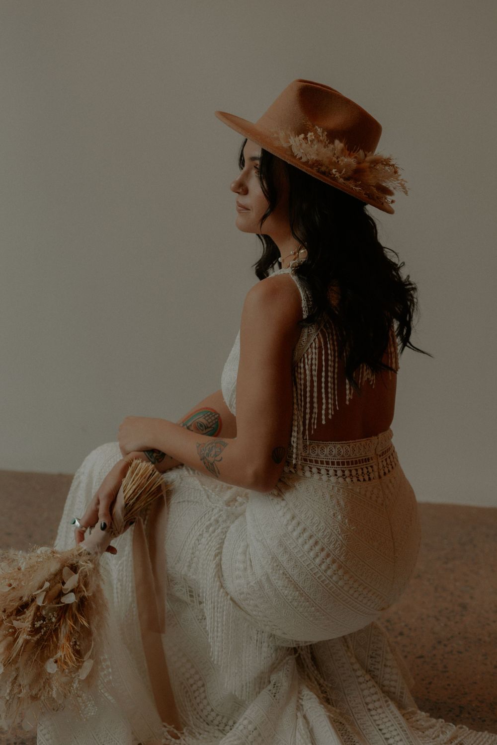 A romantic bridal portrait in white lace dress and brown hat with bohemian styling.