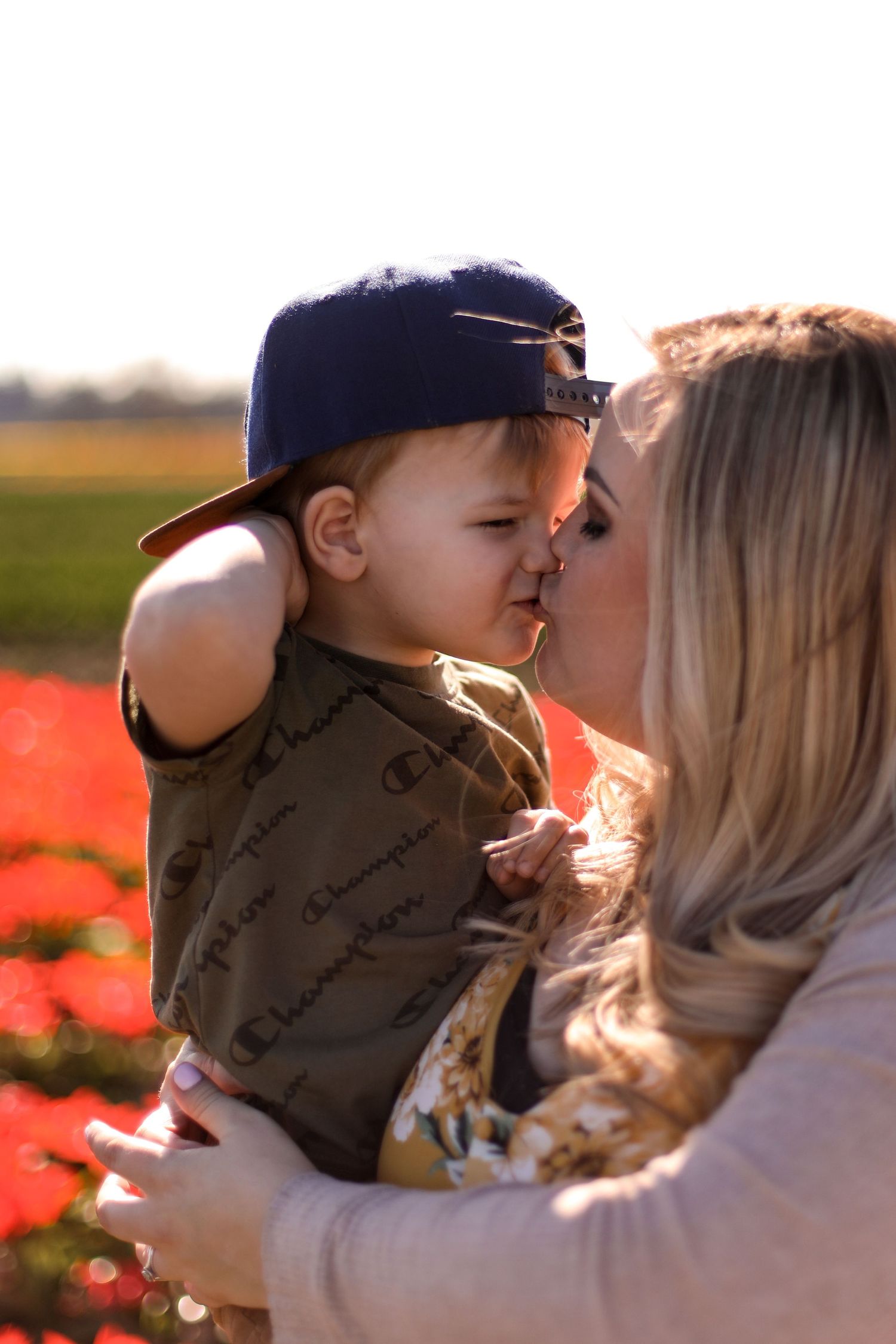 Tender moment between parent and child in baseball cap against sunset-lit field of flowers.