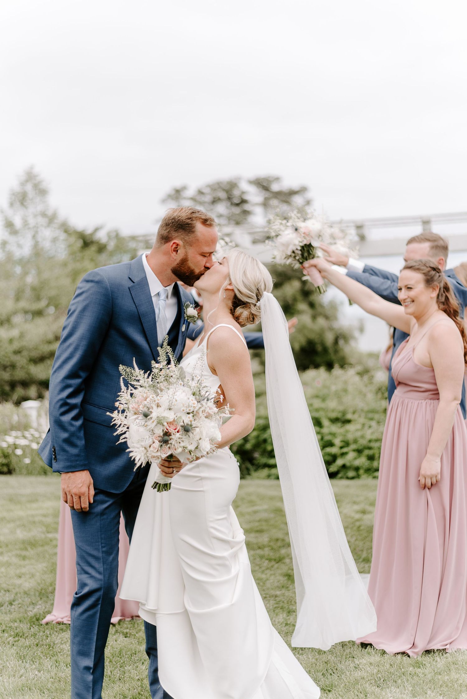 Wedding party poses outdoors with bride in white dress and bridesmaids in blush pink gowns.