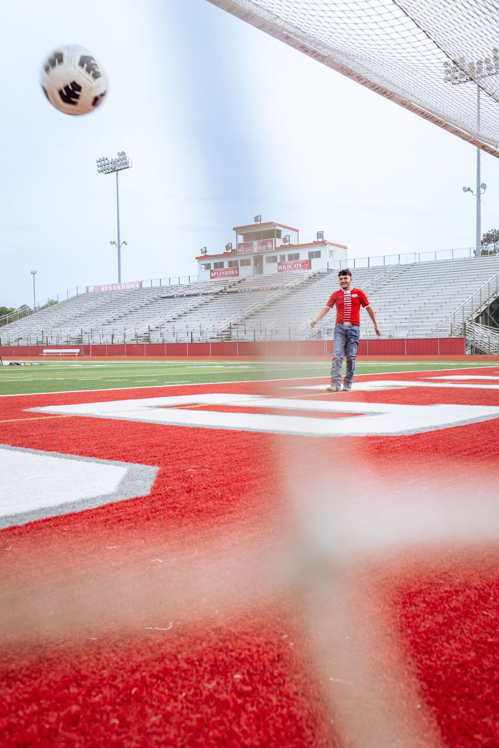 Soccer player kicking ball toward goal on red turf stadium field.