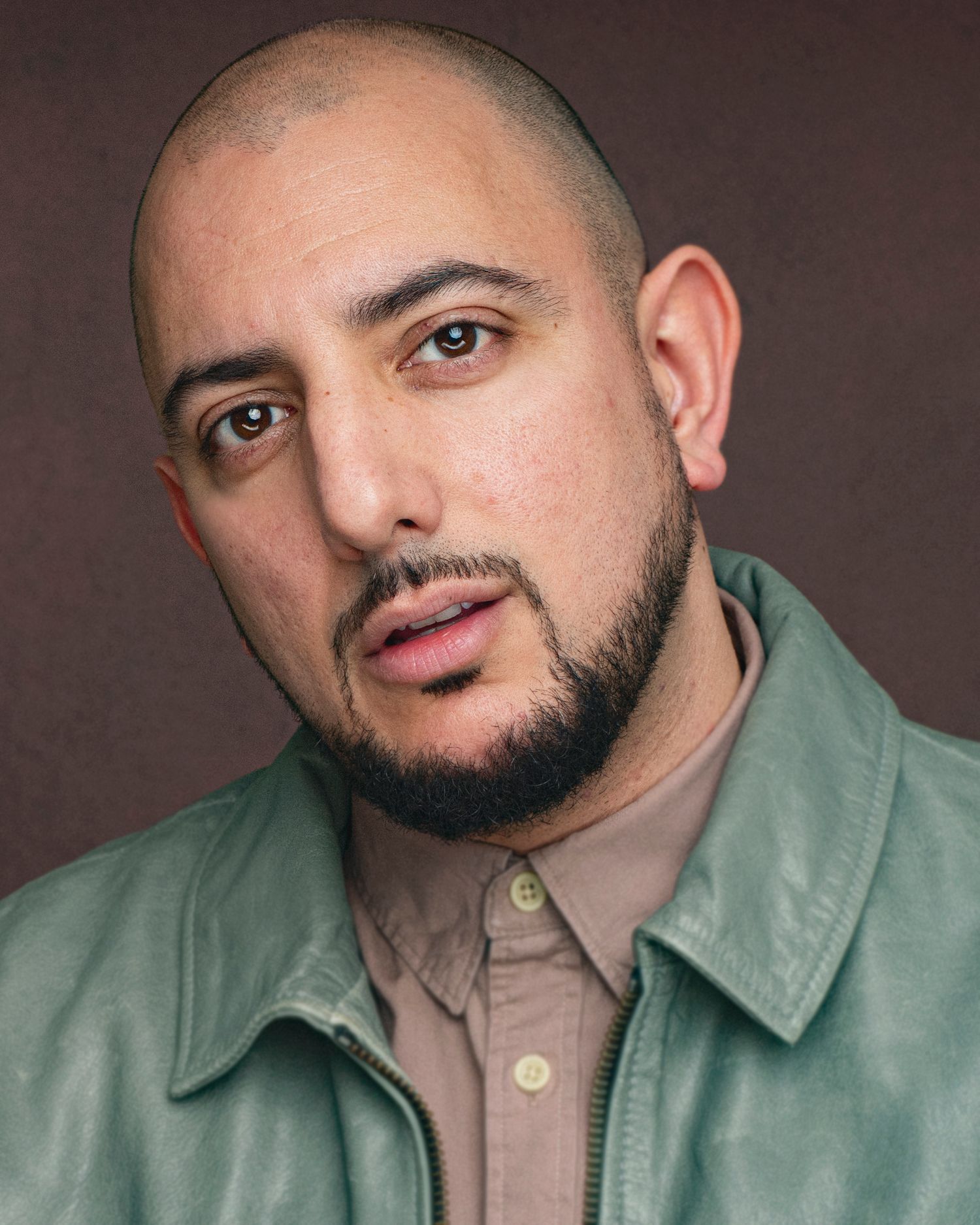 Studio headshot of person in green jacket and beige shirt against dark background.