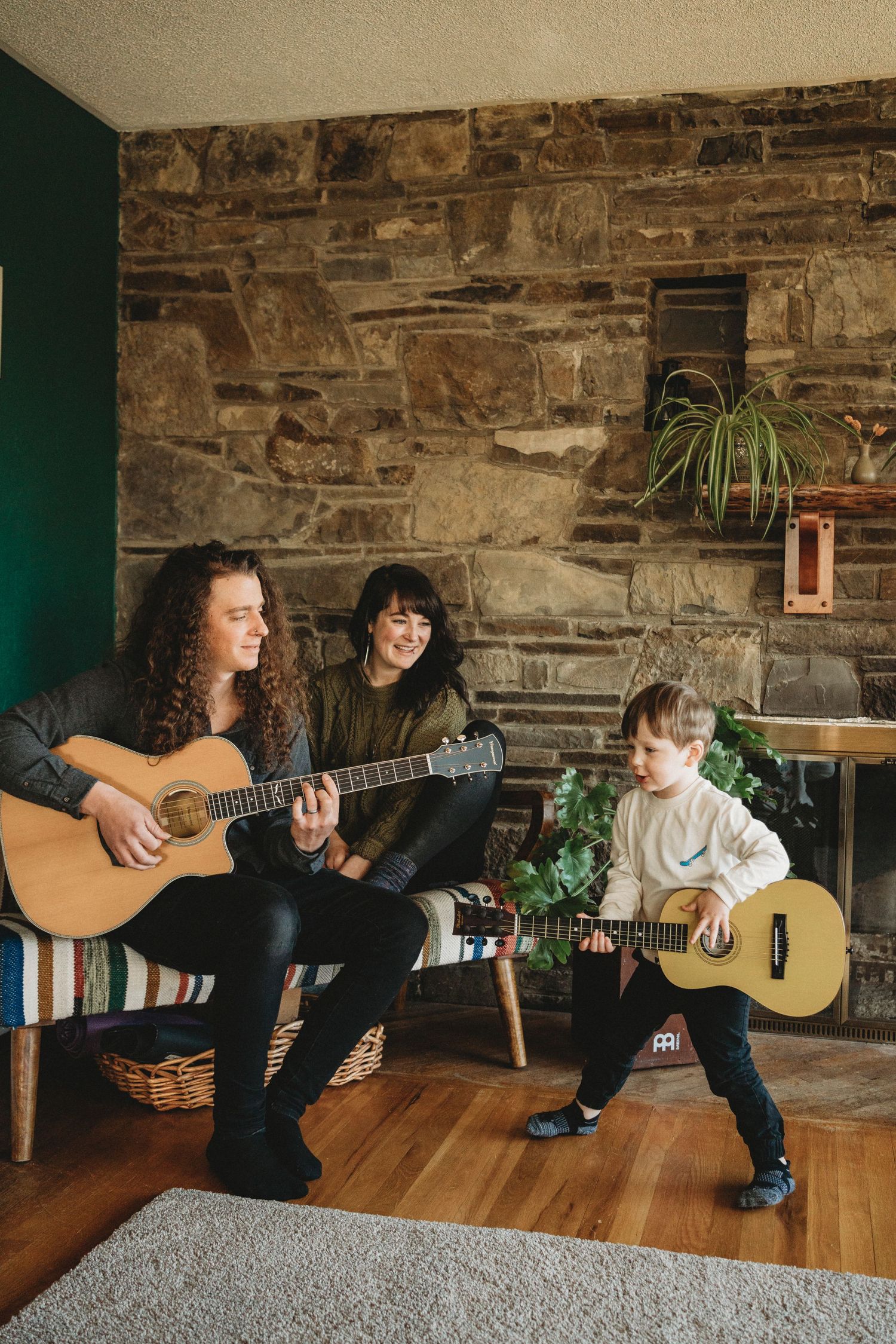 Family music session with acoustic guitars in rustic room with stone wall.