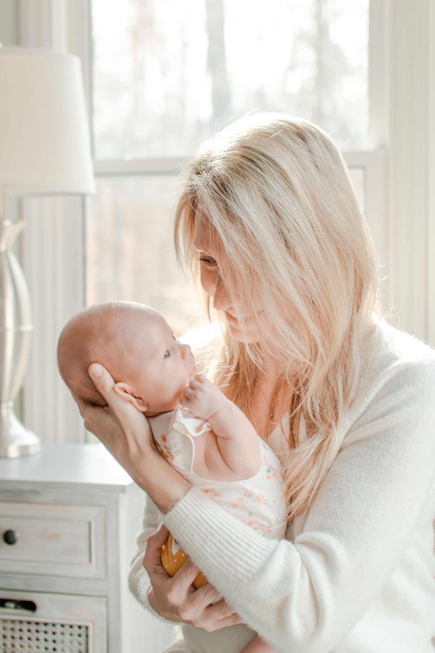 Soft backlit portrait of tender embrace between parent and infant in white cozy setting.