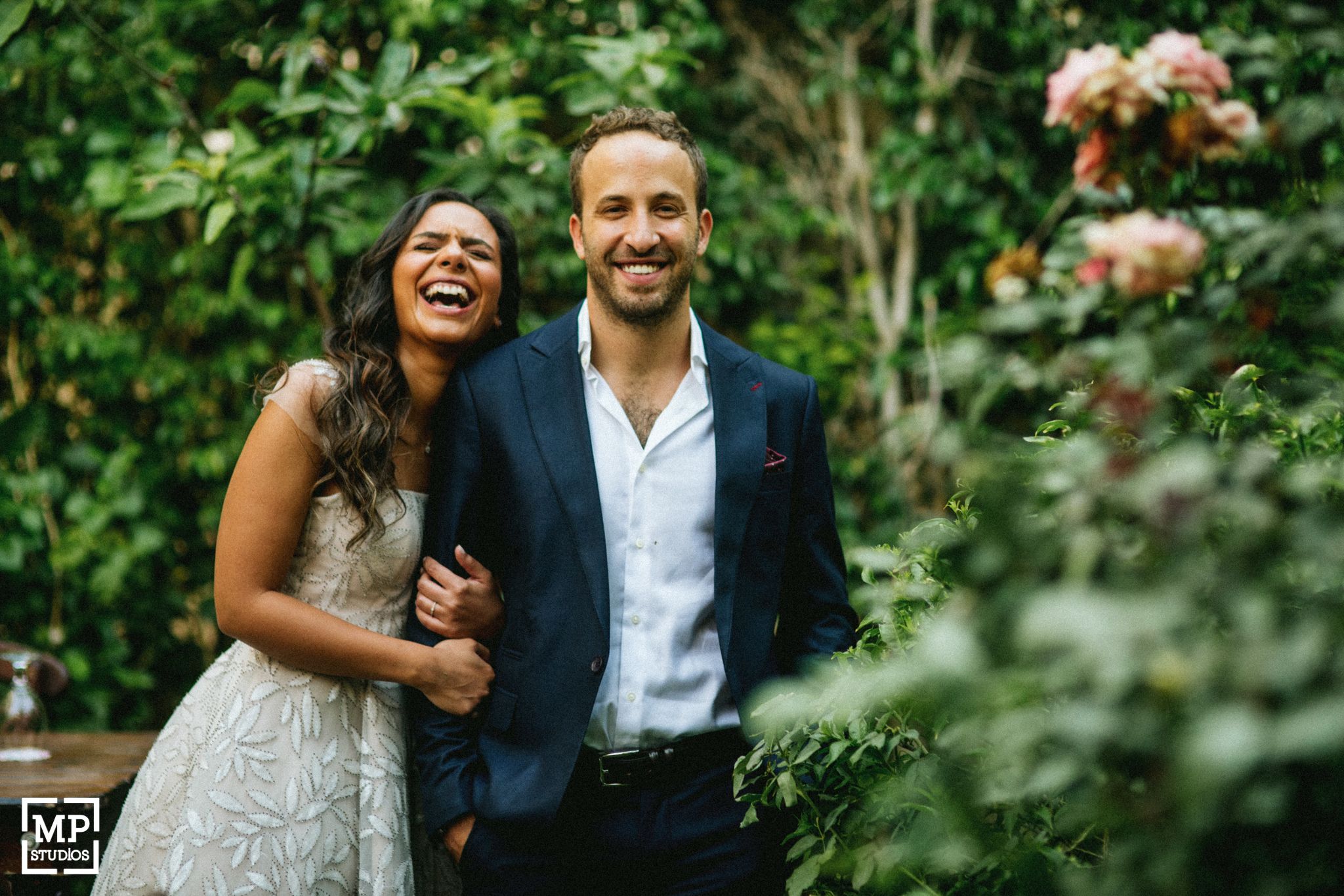 Joyful couple laughing together in garden setting with greenery background.