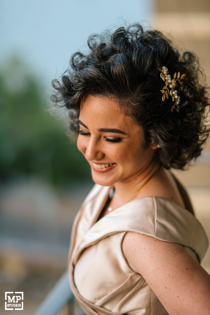 Warm portrait of curly updo hairstyle with gold floral accessory wearing beige satin dress.