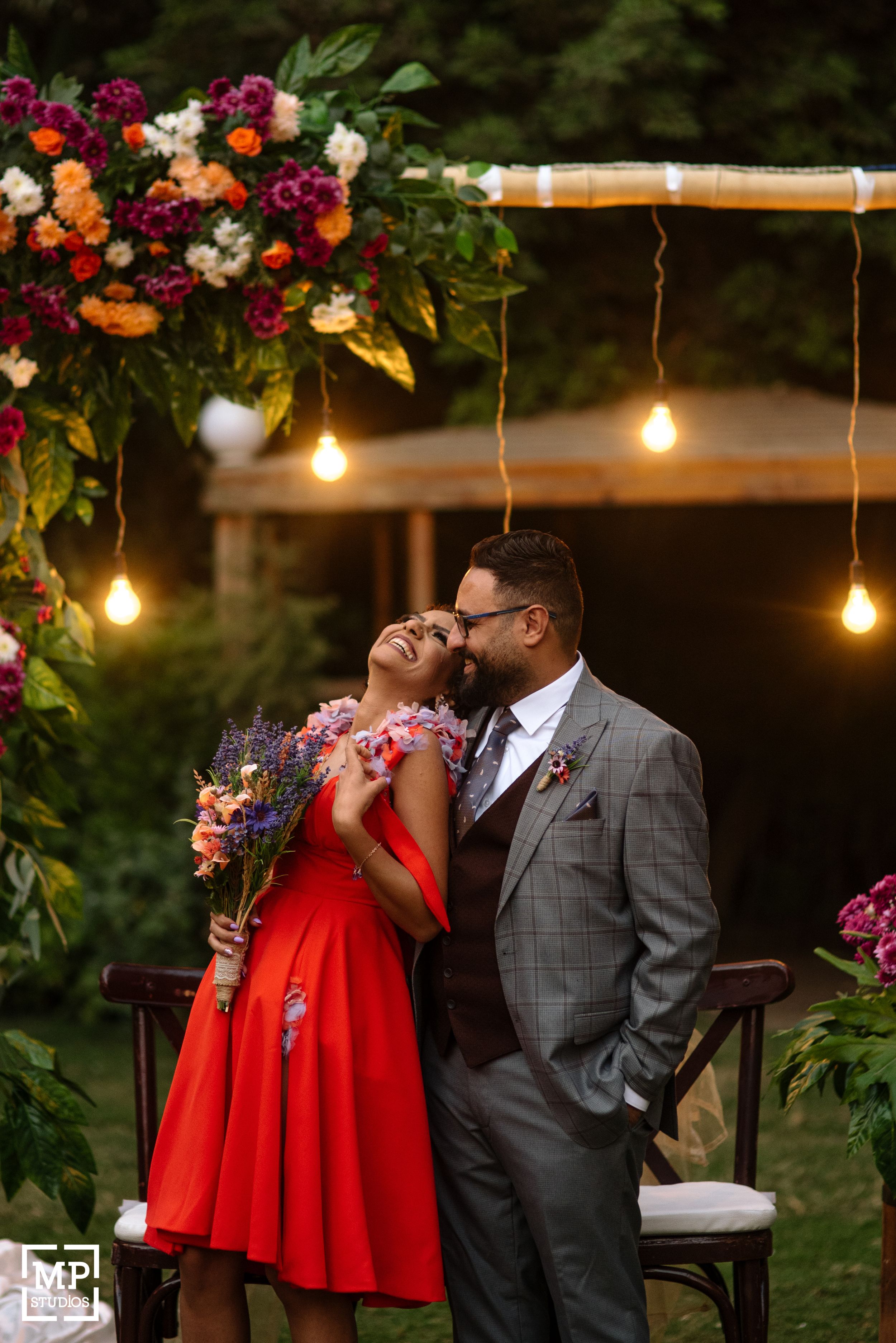 A couple embraces under hanging lights and floral arrangements in a garden setting.