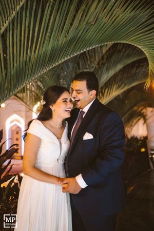 A couple shares an intimate moment under palm trees during their wedding.