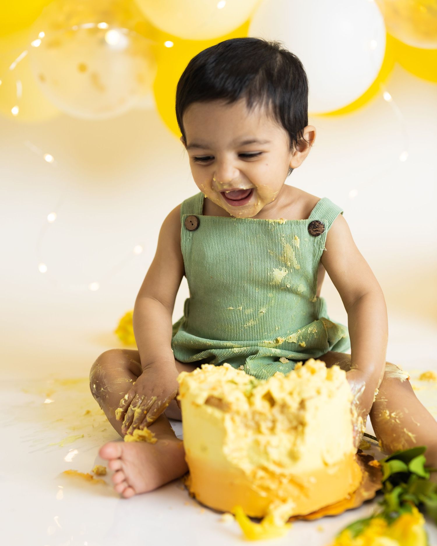 First birthday cake smash scene with yellow cake against balloon backdrop.