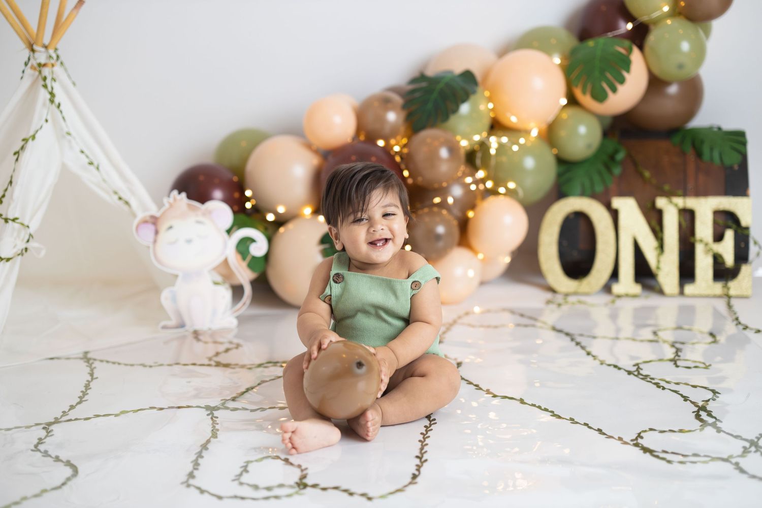 Birthday party scene with balloon arch, gold ONE letters, and unicorn decoration.