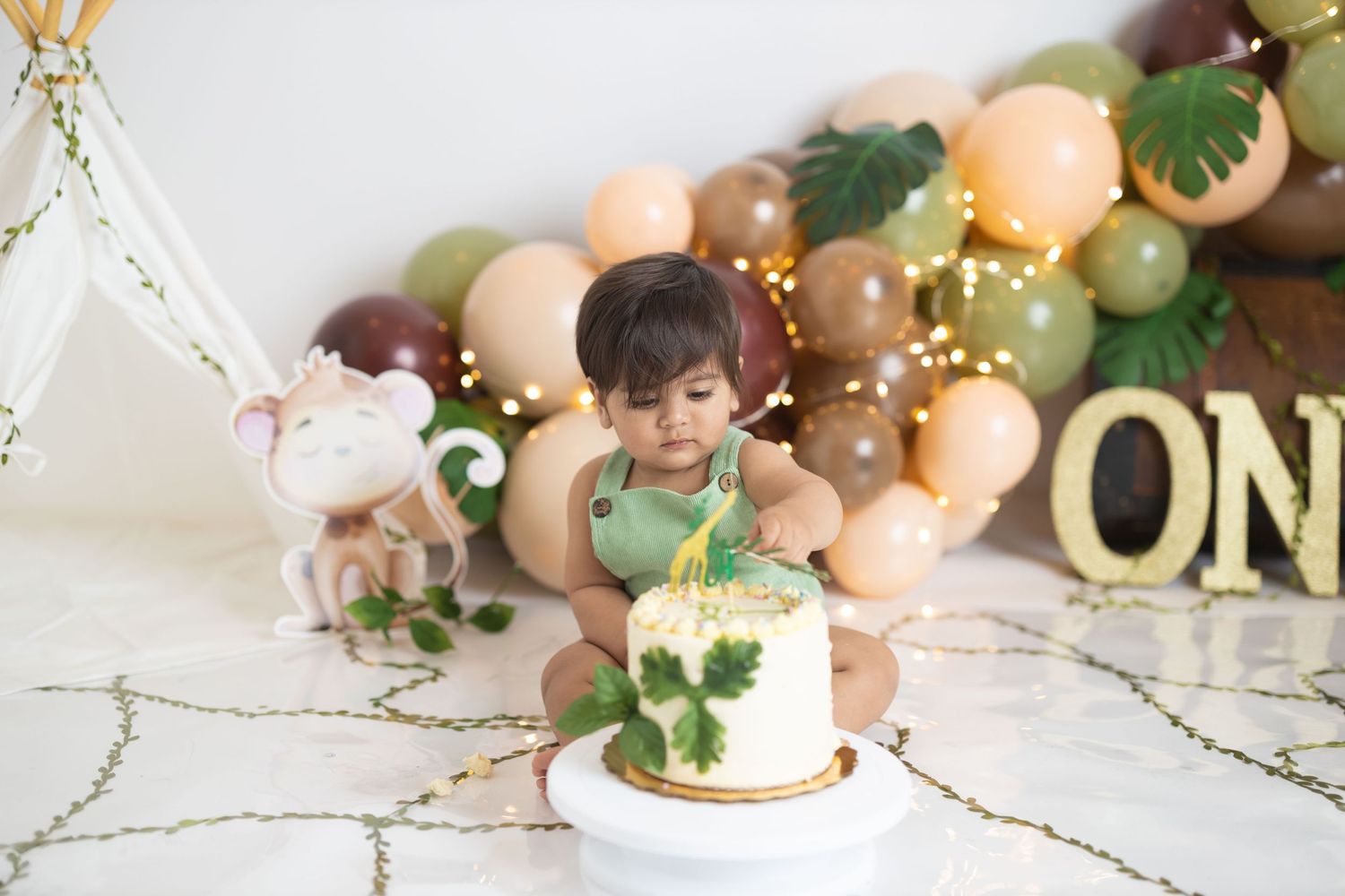 First birthday celebration with peach and green balloon garland and small white cake.