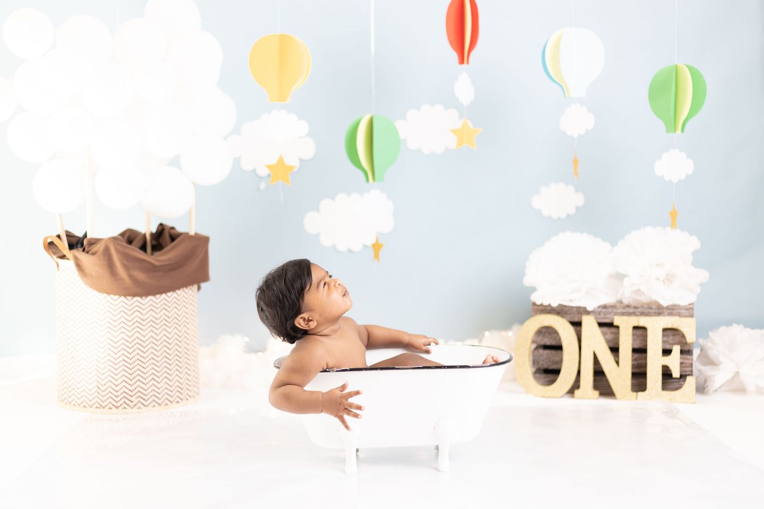 Baby in cake smash photo session with hot air balloon decorations and gold ONE letters.