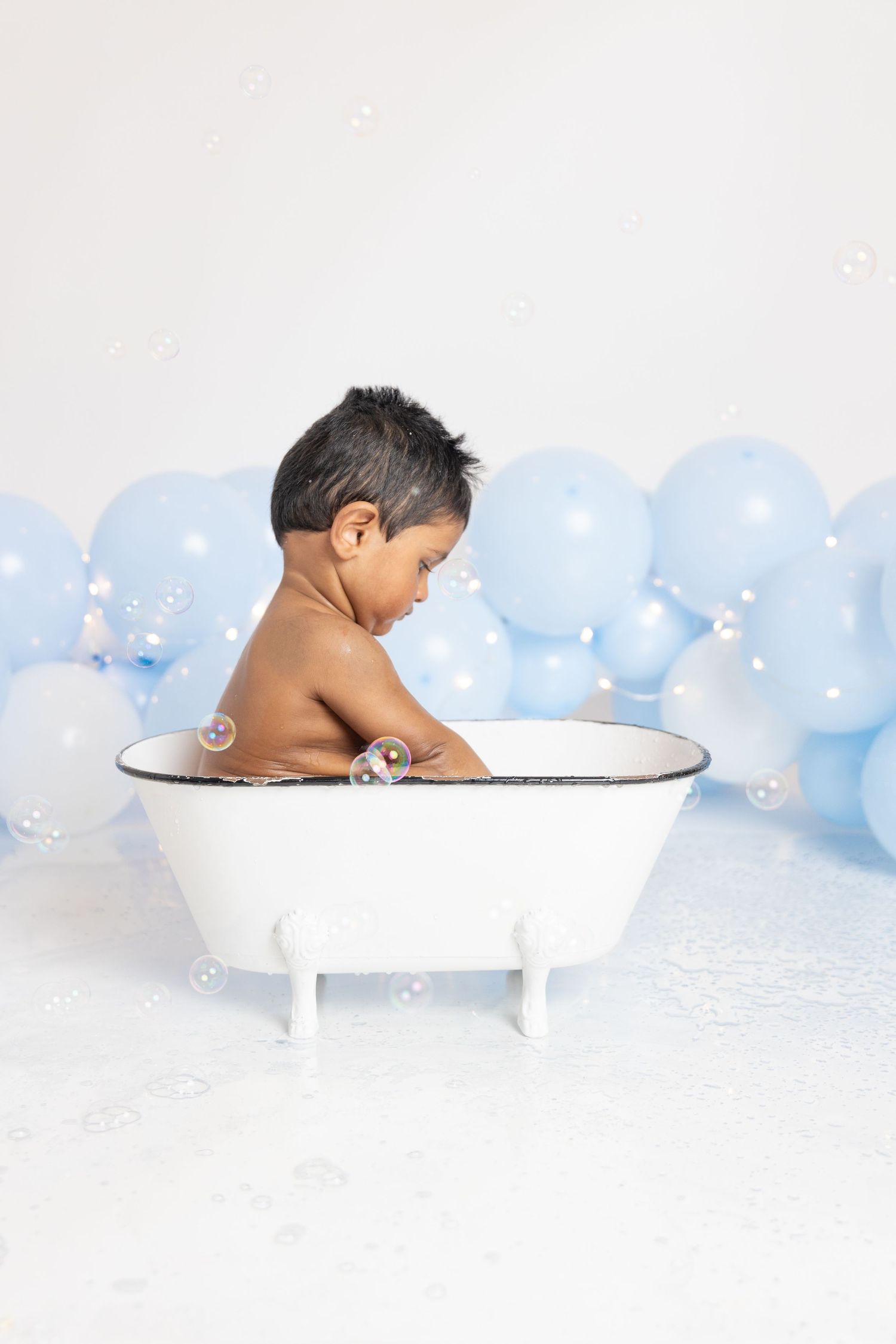Bath time photo shoot with vintage tub and blue balloon backdrop.