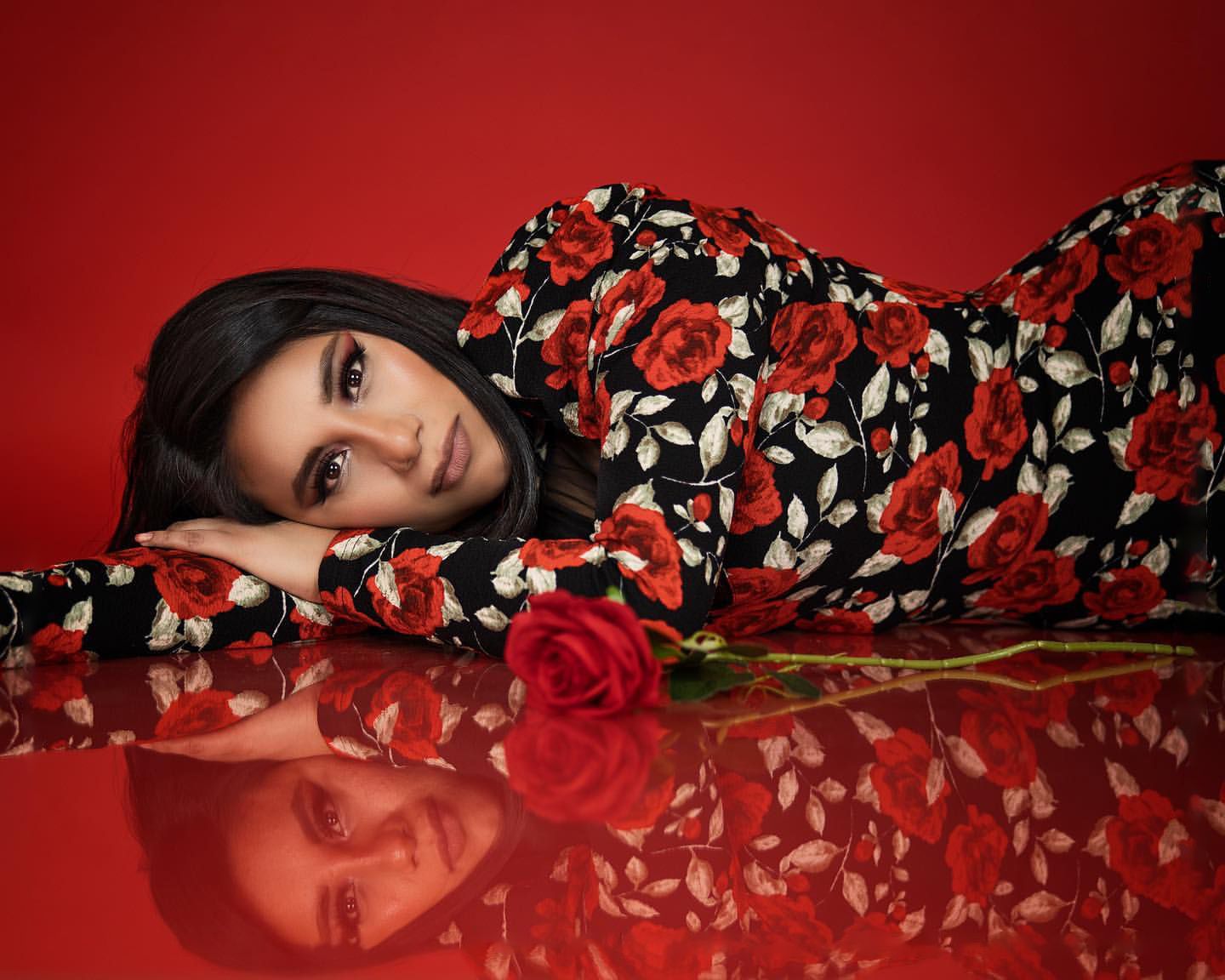 Artistic fashion portrait with floral dress and red rose against reflective red background.