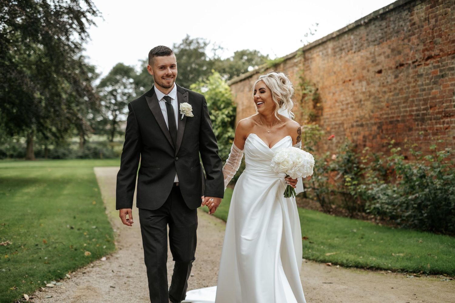 Wedding Thorpe Gardens Tamworth. Bride in white dress, groom in suit walking in walled garden smiling