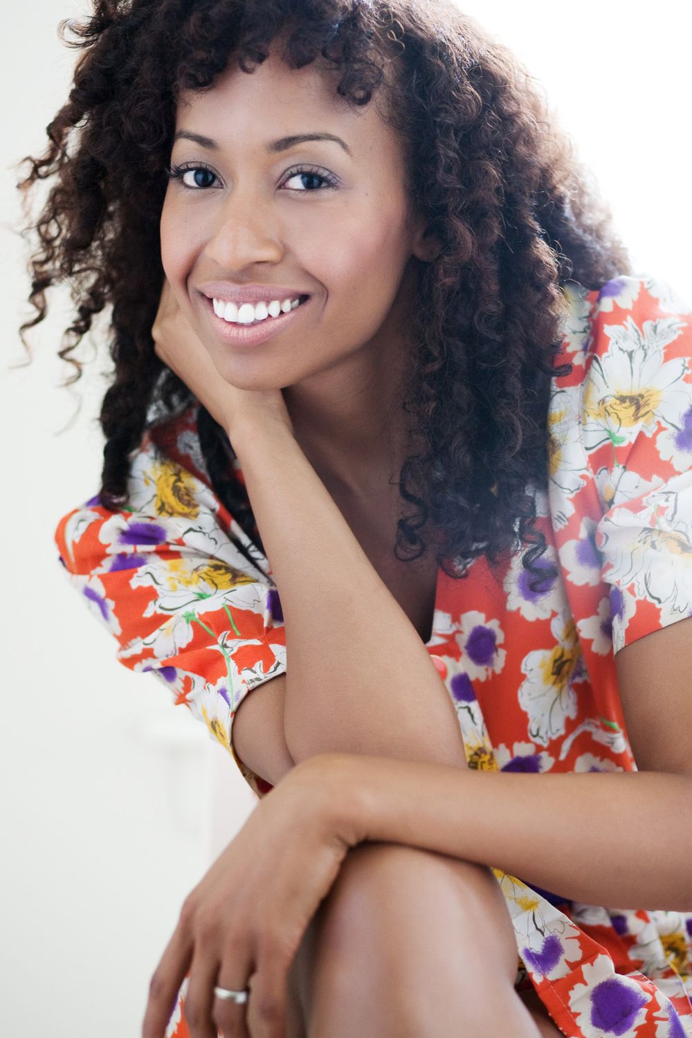 portrait of a woman with curly hair wearing a floral printed dress on a white background