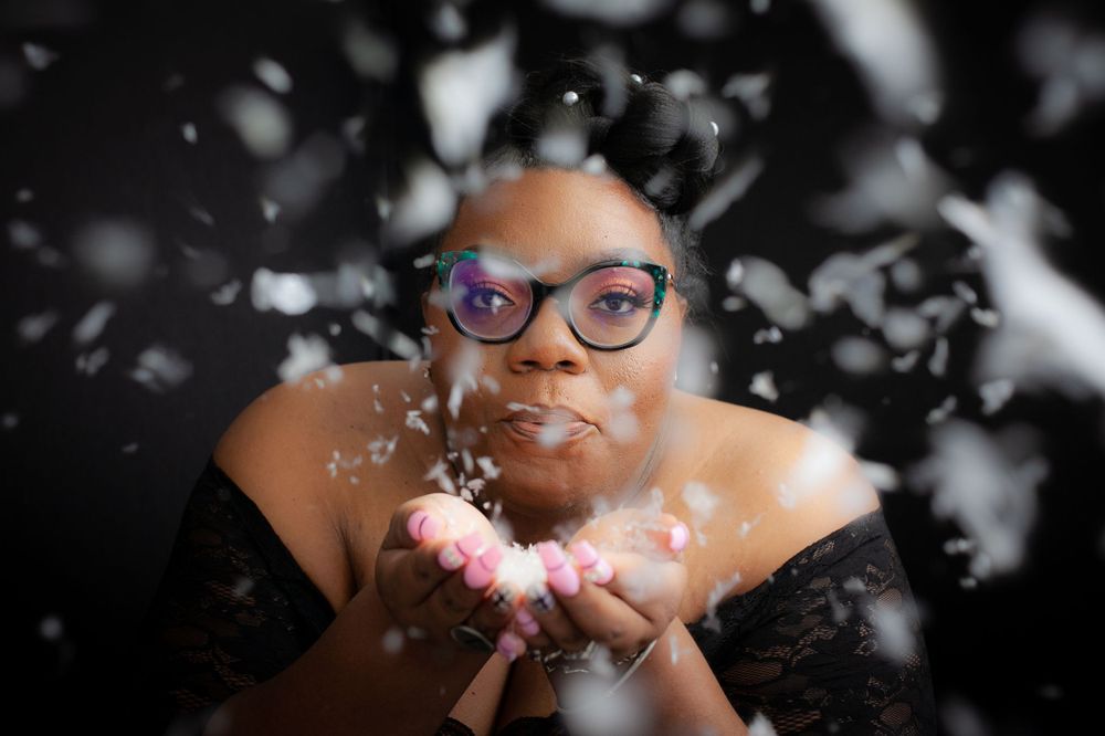 a young woman with glasses blows snowflakes towards the camera