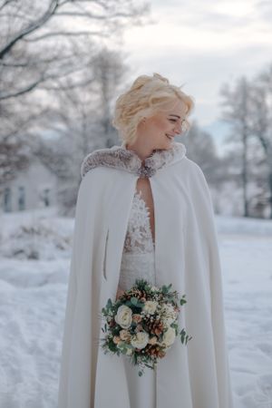 Hochzeitsfotografie: Braut steht im Schnee und hält einen winterlichen Blumenstrauß, aufgenommen im Raum Freising.