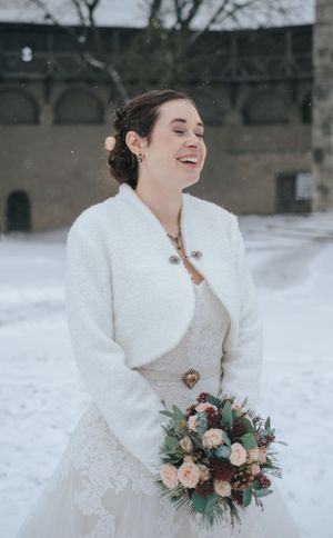 Hochzeitsfotografie: Braut steht lachend im Schnee und hält einen Blumenstrauß, Winterhochzeit im Raum Dachau.