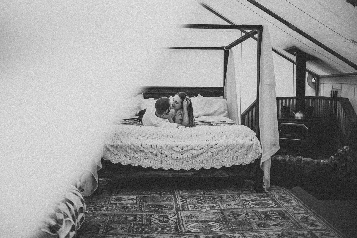 A black and white image of a couple laying together on a bed inside a tent.