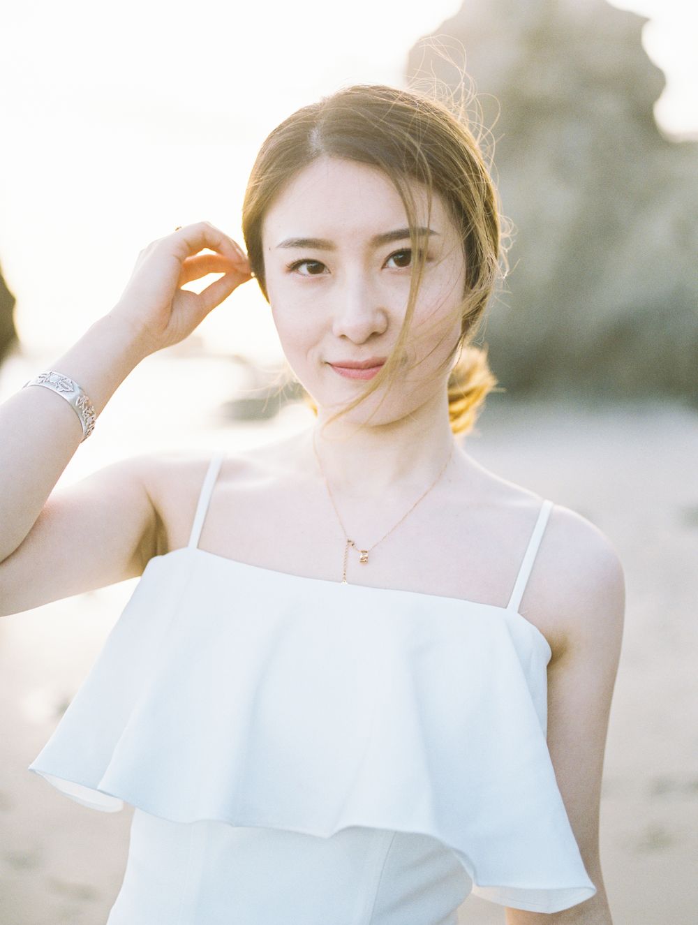 Woman in white camisole top with sunlit glow at beach.