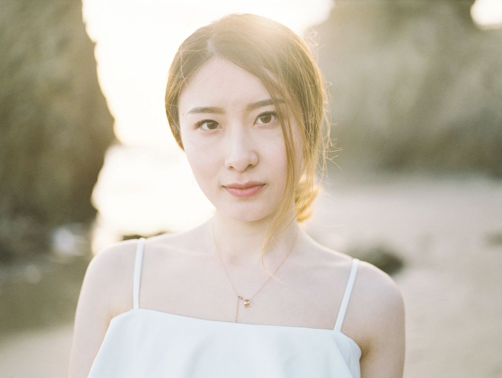Woman in white summer top with sunlit glow against beach backdrop.