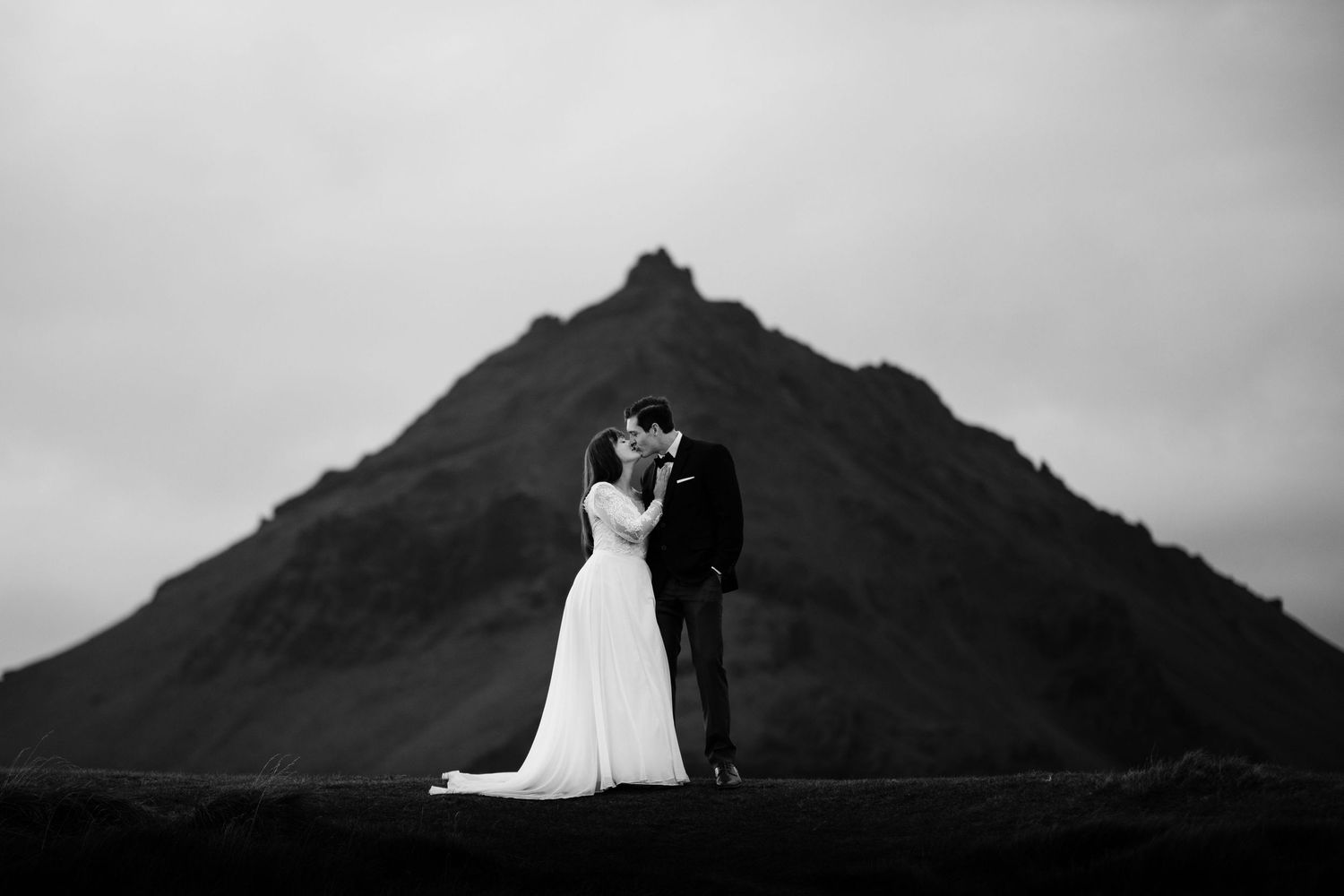 Silhouetted figures stand before a dramatic mountain peak under moody skies.
