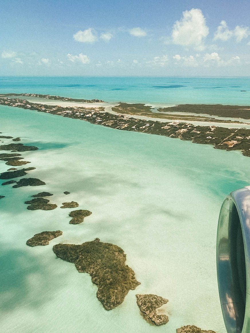 Aerial view of tropical islands and turquoise waters with part of an aircraft wing visible.