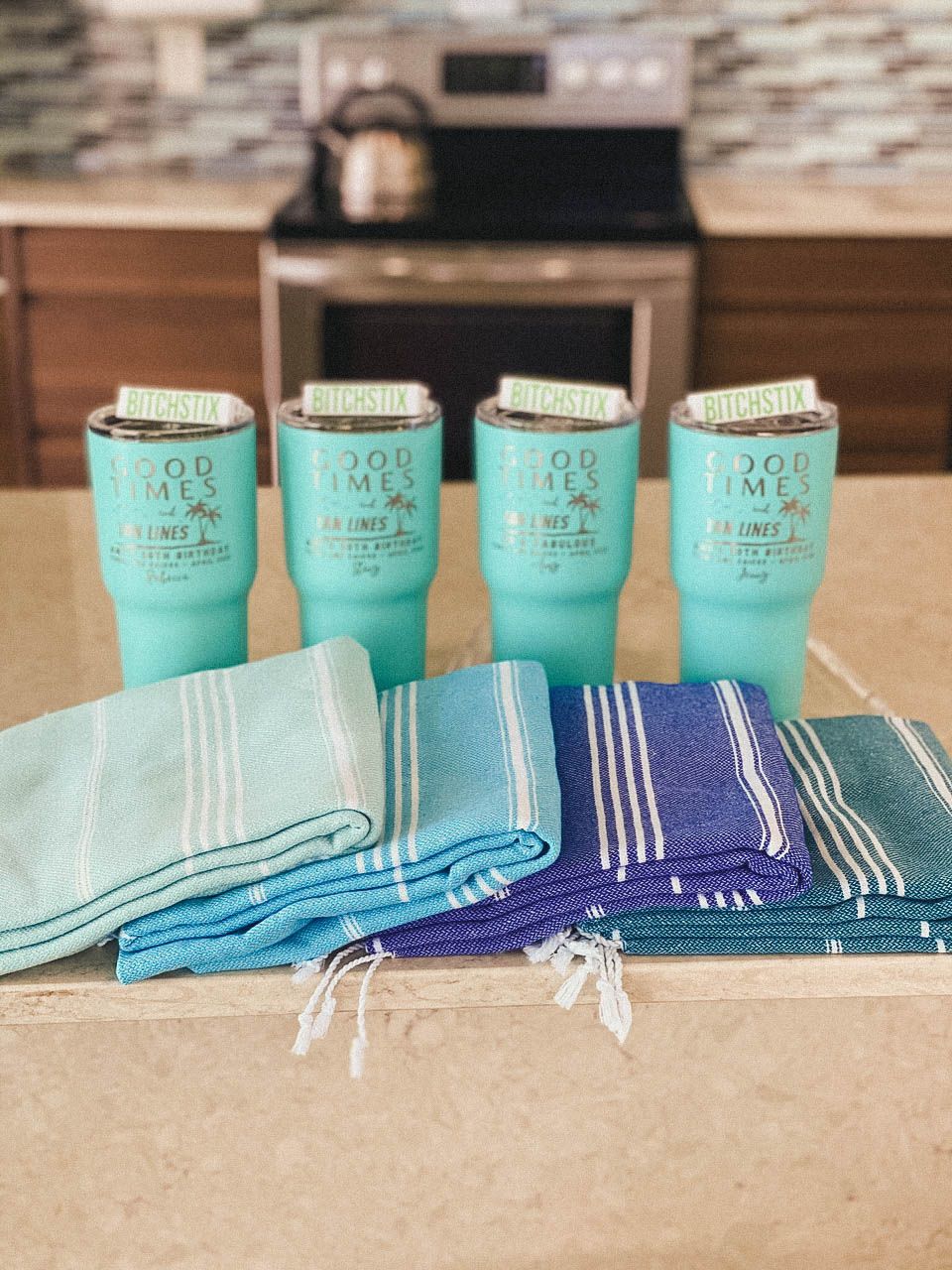 Row of matching turquoise cups and blue striped towels arranged on wooden surface.