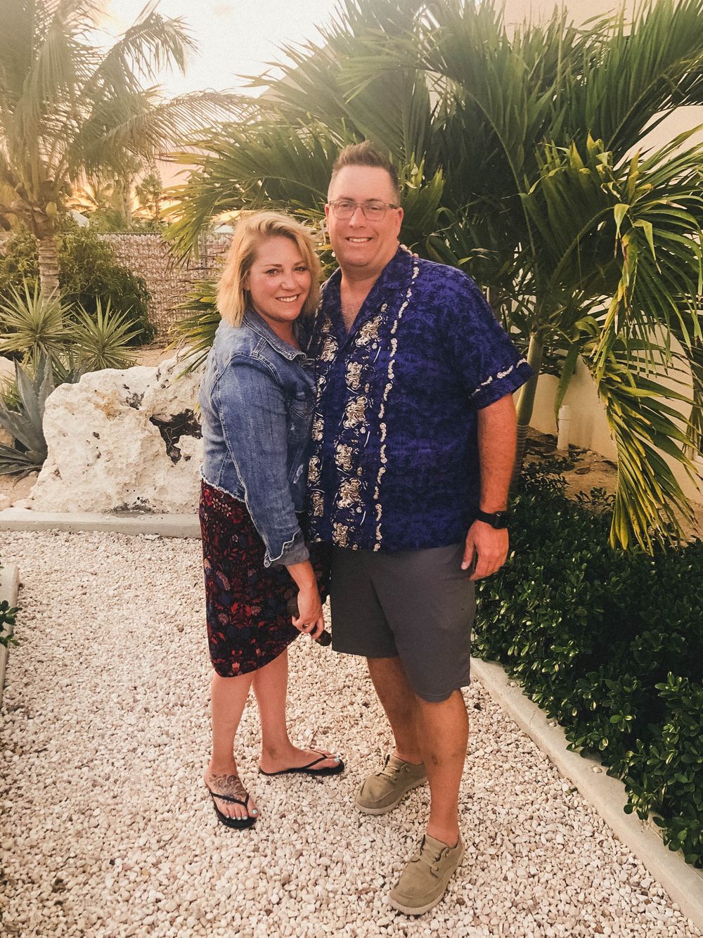 Couple poses together on a tropical pathway surrounded by palm trees and white stones.