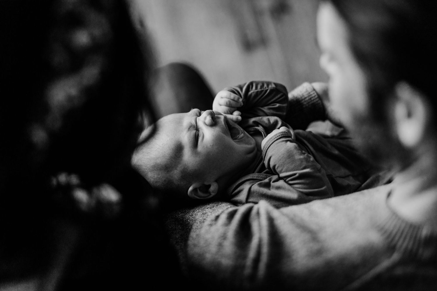 A tiny baby yawns while being cradled in black and white portrait photography.