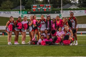 Cheerleading squad poses together on football field wearing pink and black uniforms.