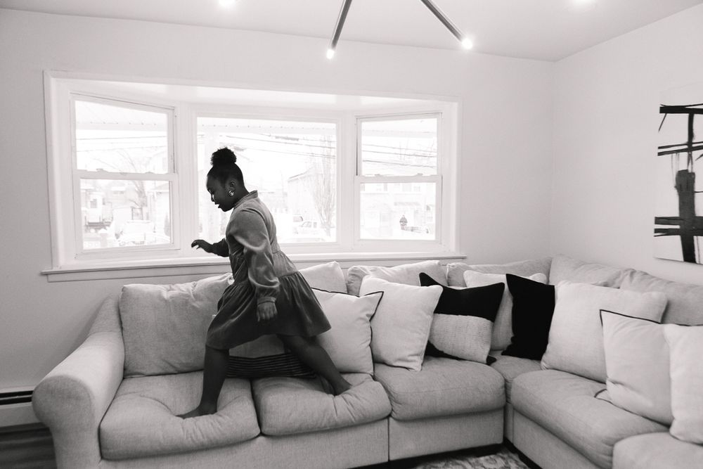 a black and white view of a girl jumping on the couch during a family session in Queens by Paula Ortiz NYC family photos
