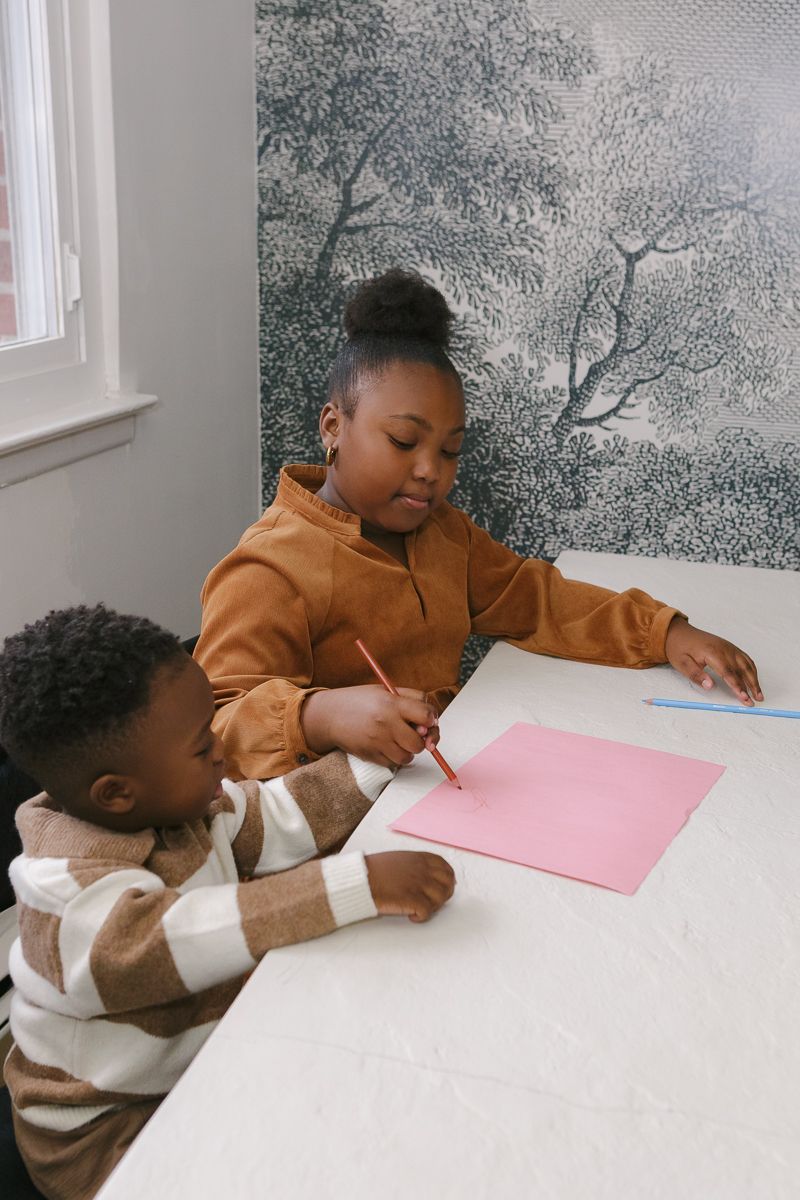 a girl and his little brother draw together at the dinning table during a family photoshoot in Queens, NY