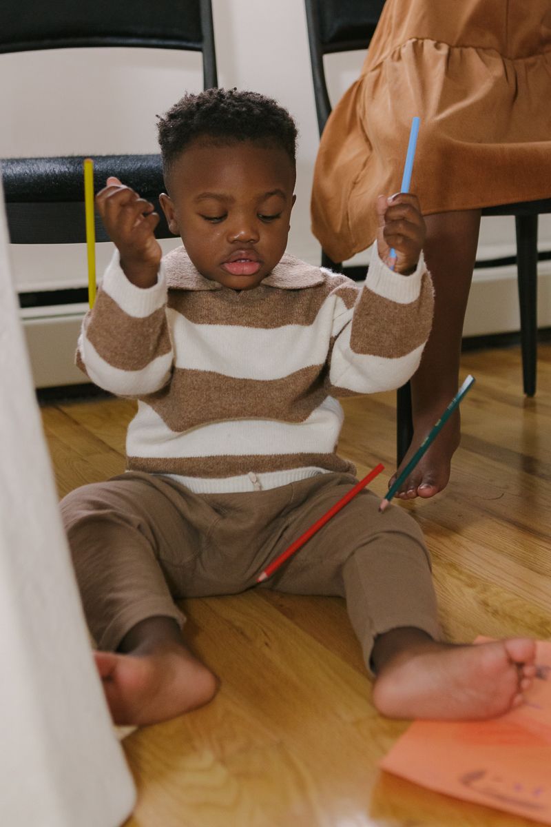 a little boy plays with color pencils under the table candidly during an in home family session in Queens by Paula Ortiz