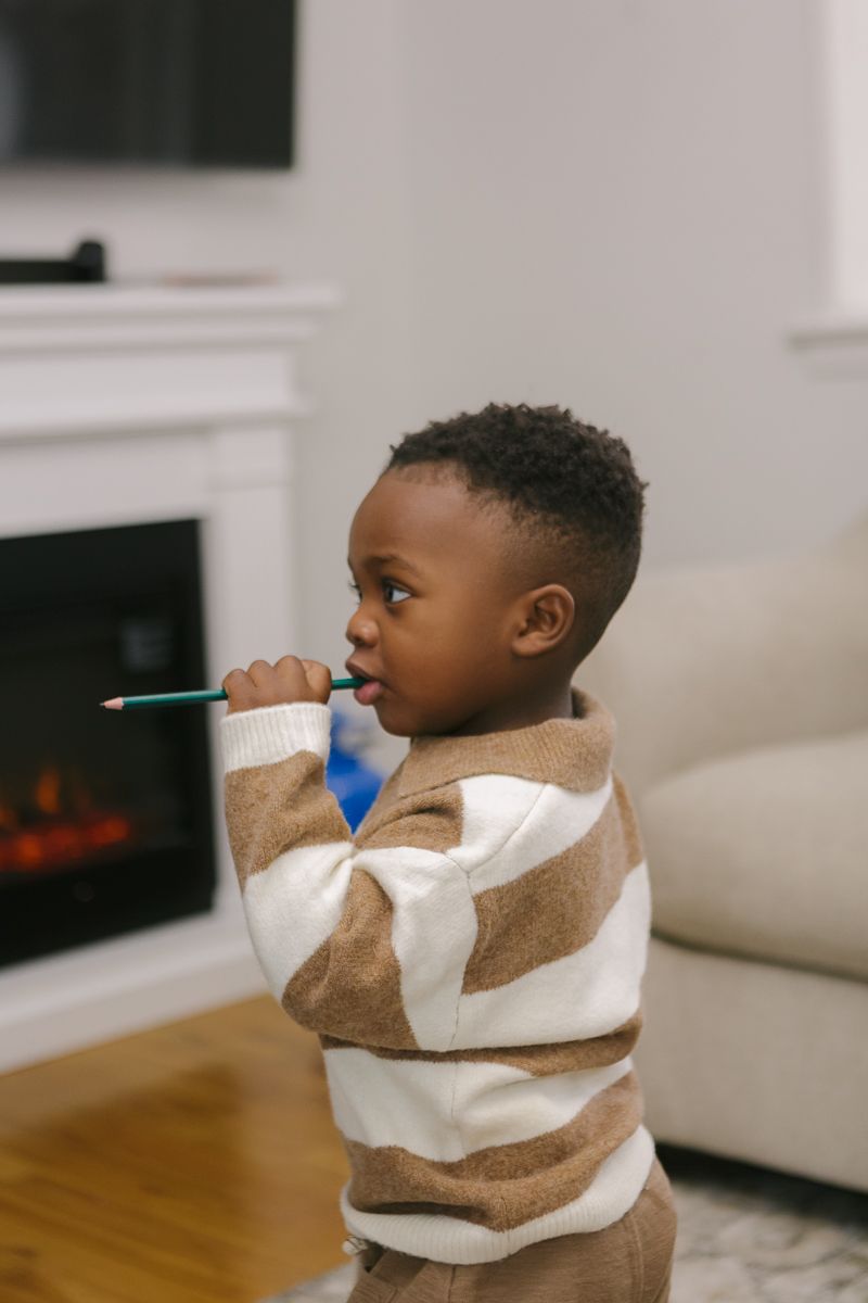 a toddler boy bites a pencil candidly during a family session at home by Queens family photographer Paula Ortiz