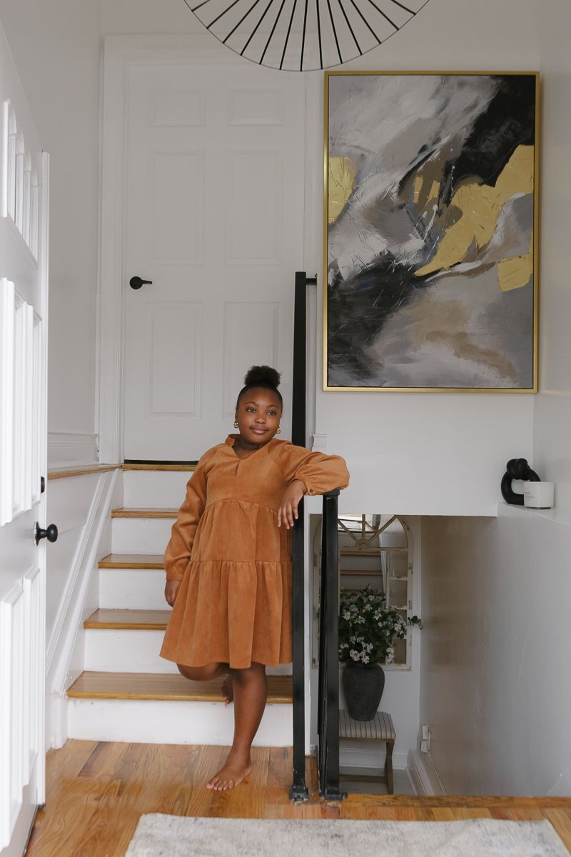 a full body view of a girl on a mustard dress standing by the front door of her new home during a session by NYC family
