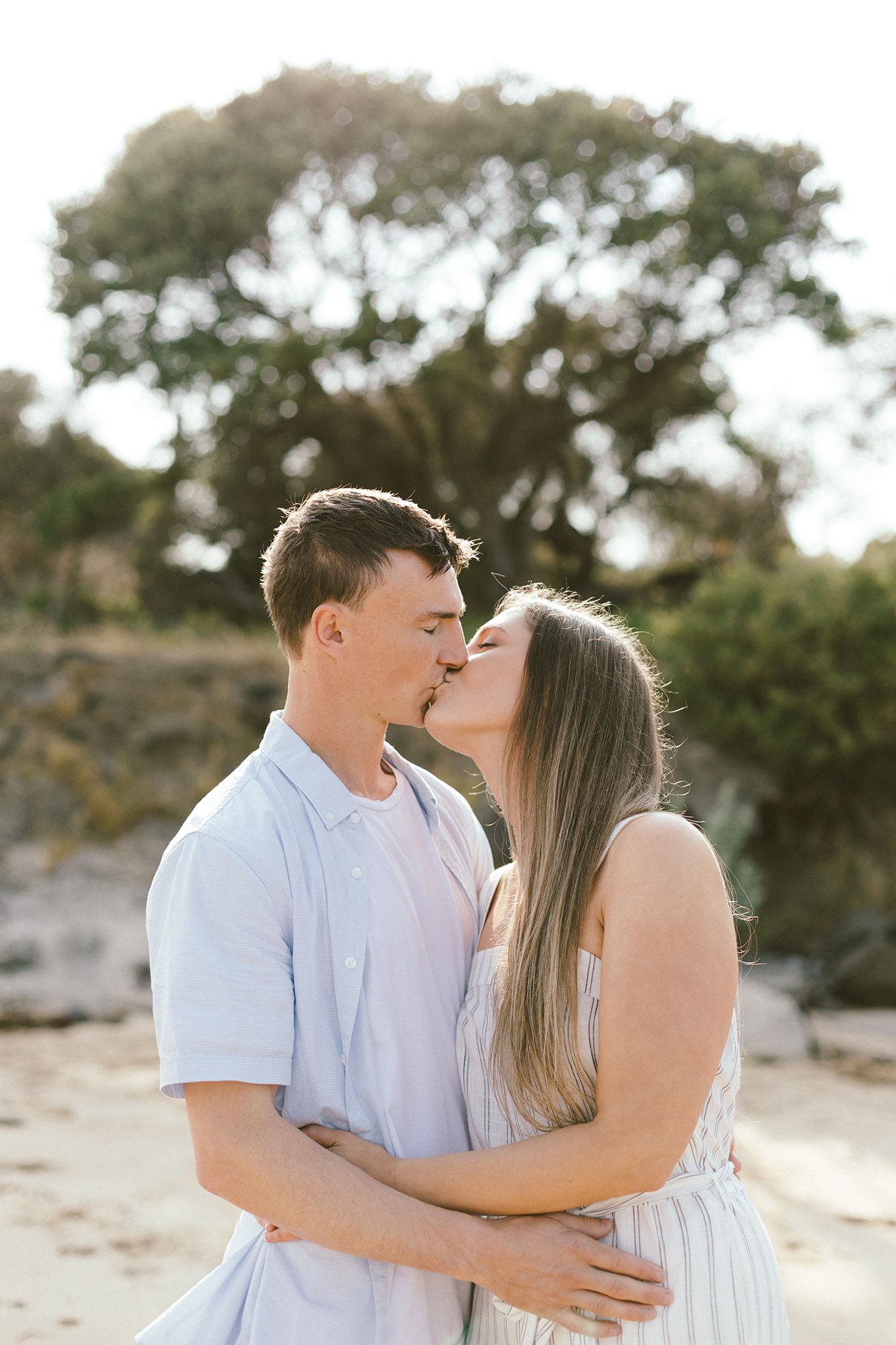 A couple shares an intimate moment on a beach during sunset.