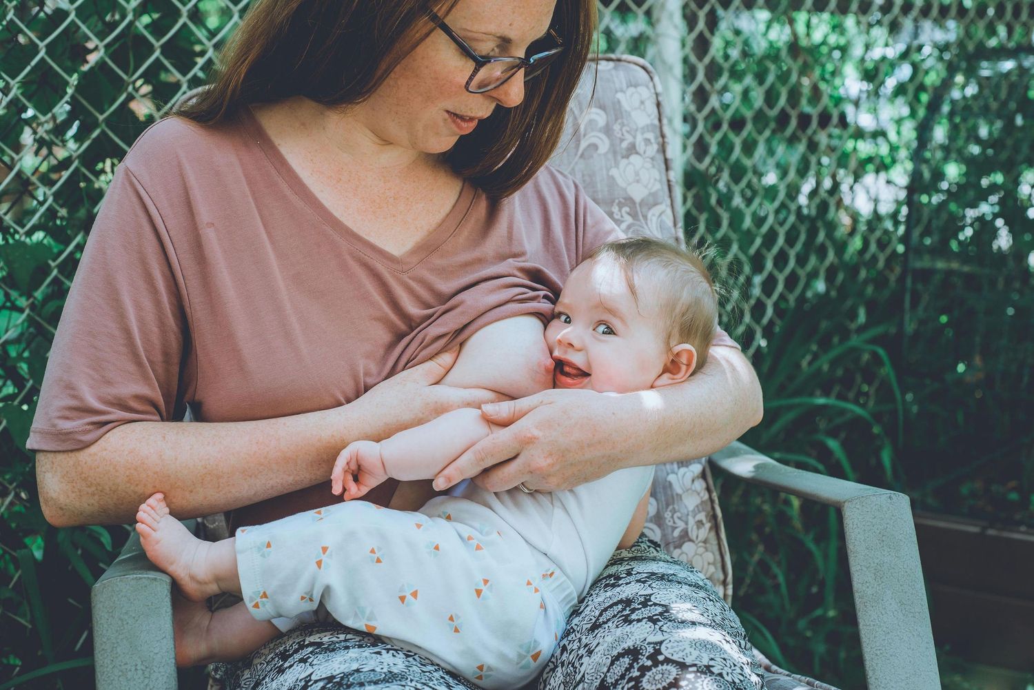 A tender moment between parent and baby sitting outdoors against a wire fence background.