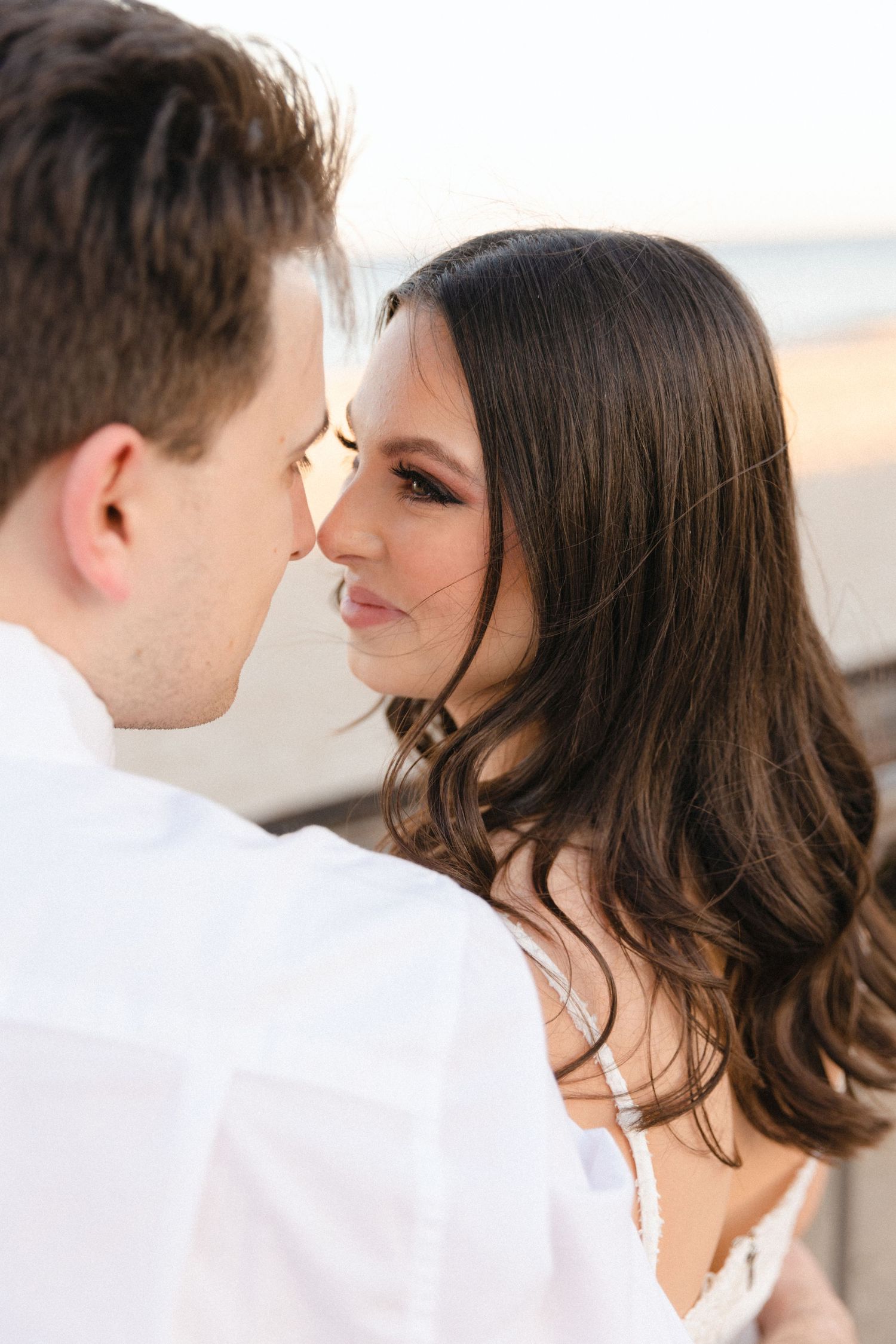Close-up of a brunette woman and her partner sharing an intimate moment during a beach engagement session.