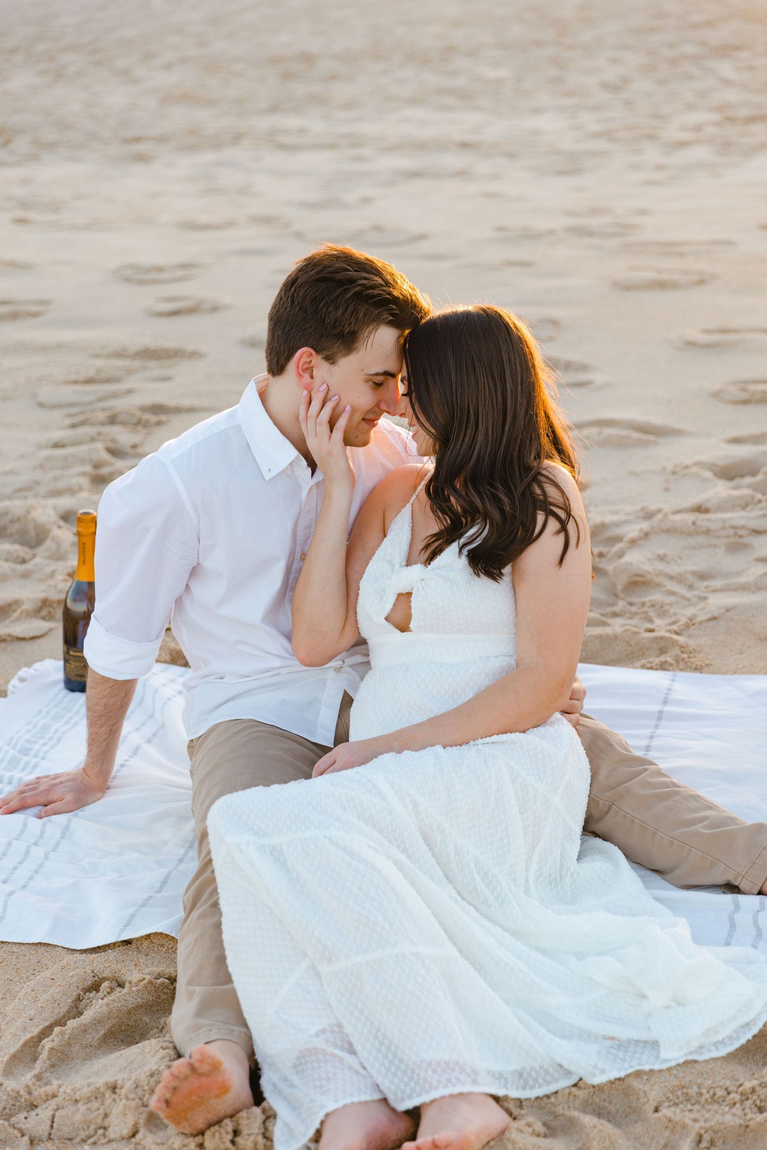 Couple sharing a romantic almost-kiss while sitting on a blanket during a warm sunset beach picnic.