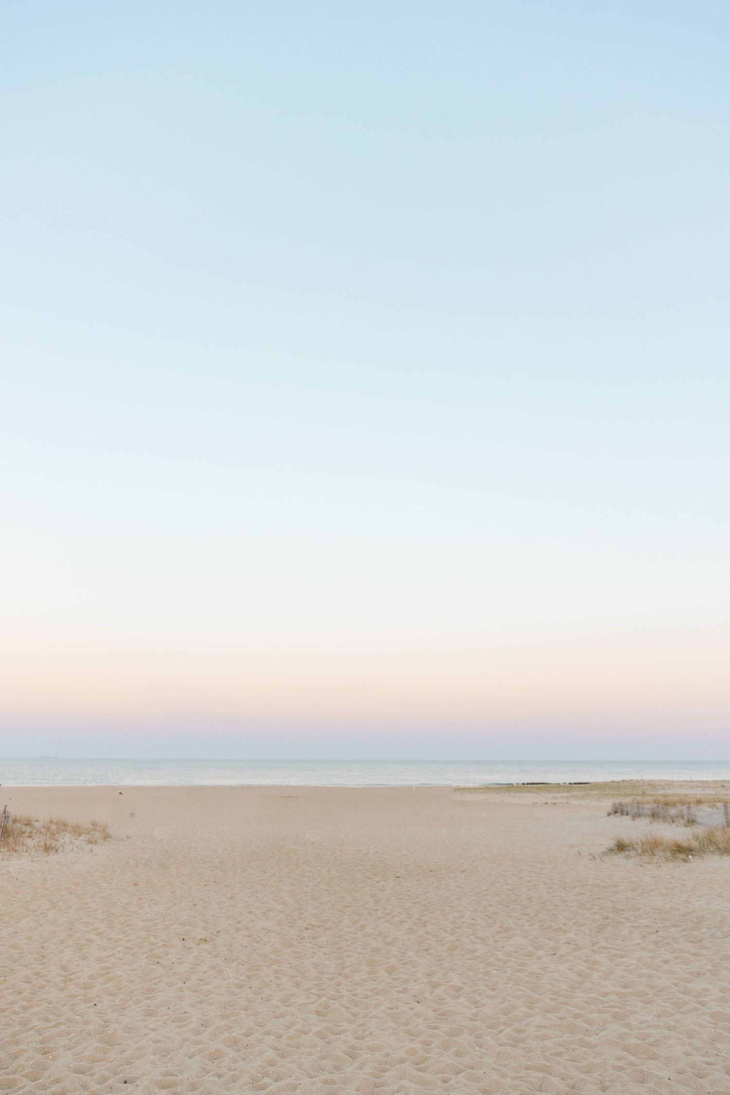 Serene empty beach scene at dusk with soft pastel pink and blue sky over calm ocean horizon.
