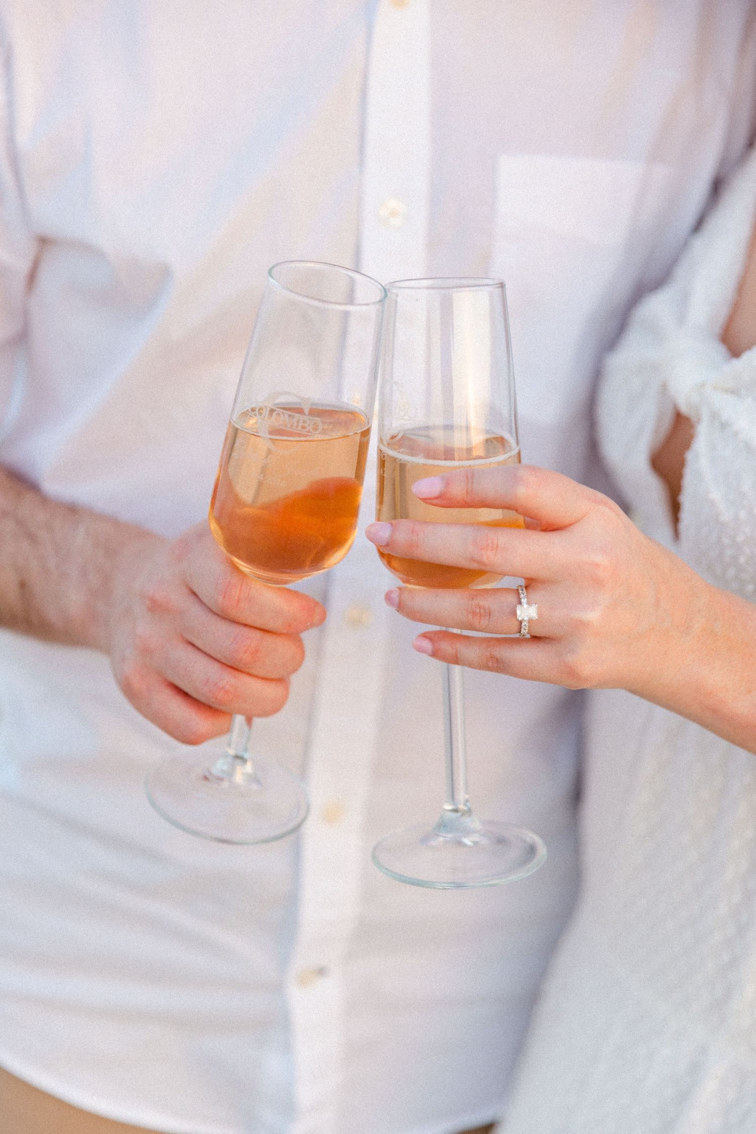 Close-up of an engaged couple toasting with champagne flutes, woman wearing a diamond engagement ring.