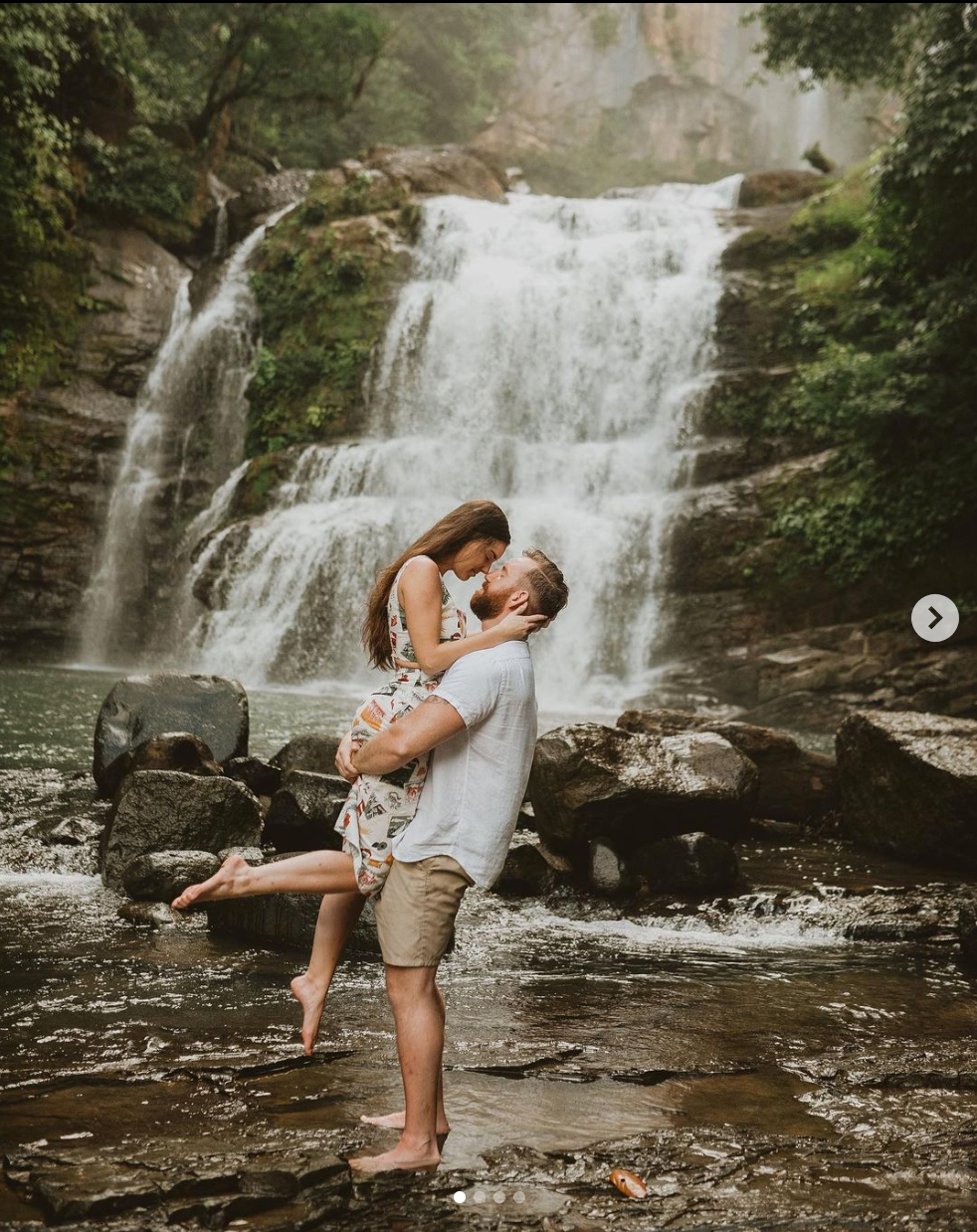 Romantic moment captured in front of majestic waterfall with couple embracing on rocks.